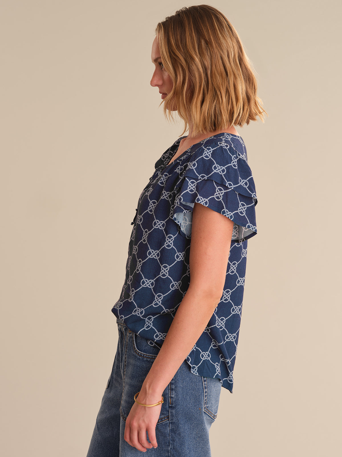 Woman wearing a blue patterned shirt and jeans on a beige background