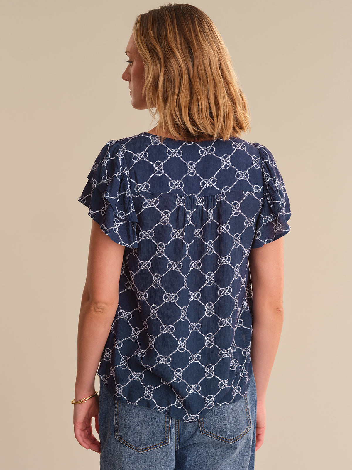 Woman wearing a navy blue patterned top and jeans on a beige background