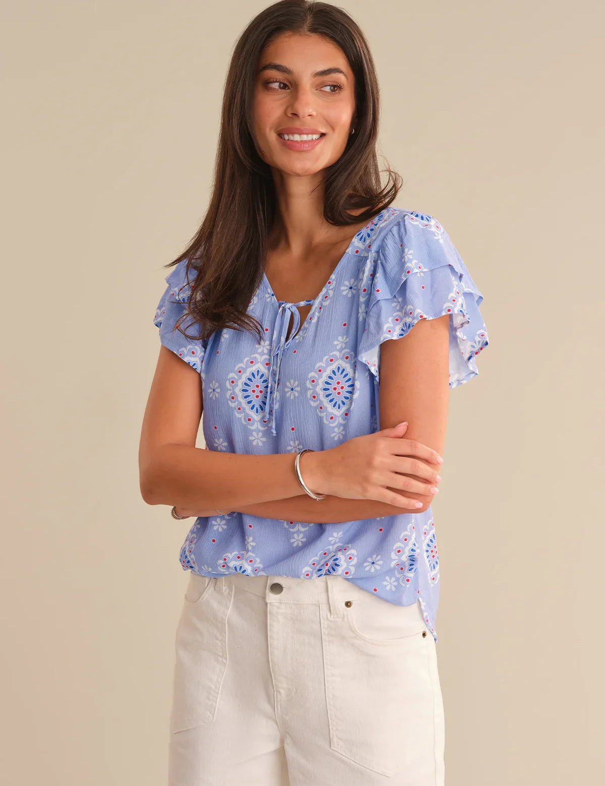 Woman wearing a blue floral blouse with white pants on a beige background