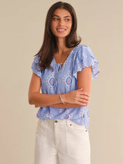 Woman wearing a blue floral blouse with white pants on a beige background