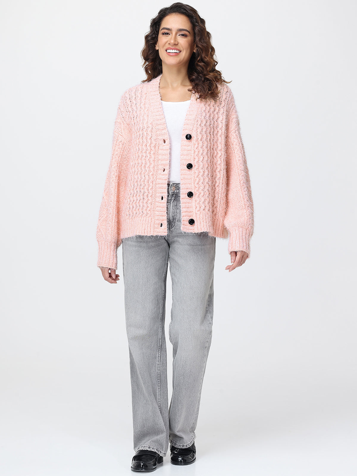 Woman wearing a pink textured cardigan over a white shirt with gray jeans on a white background