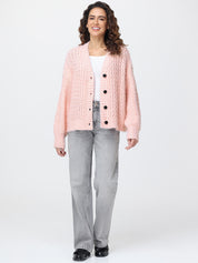 Woman wearing a pink textured cardigan over a white shirt with gray jeans on a white background