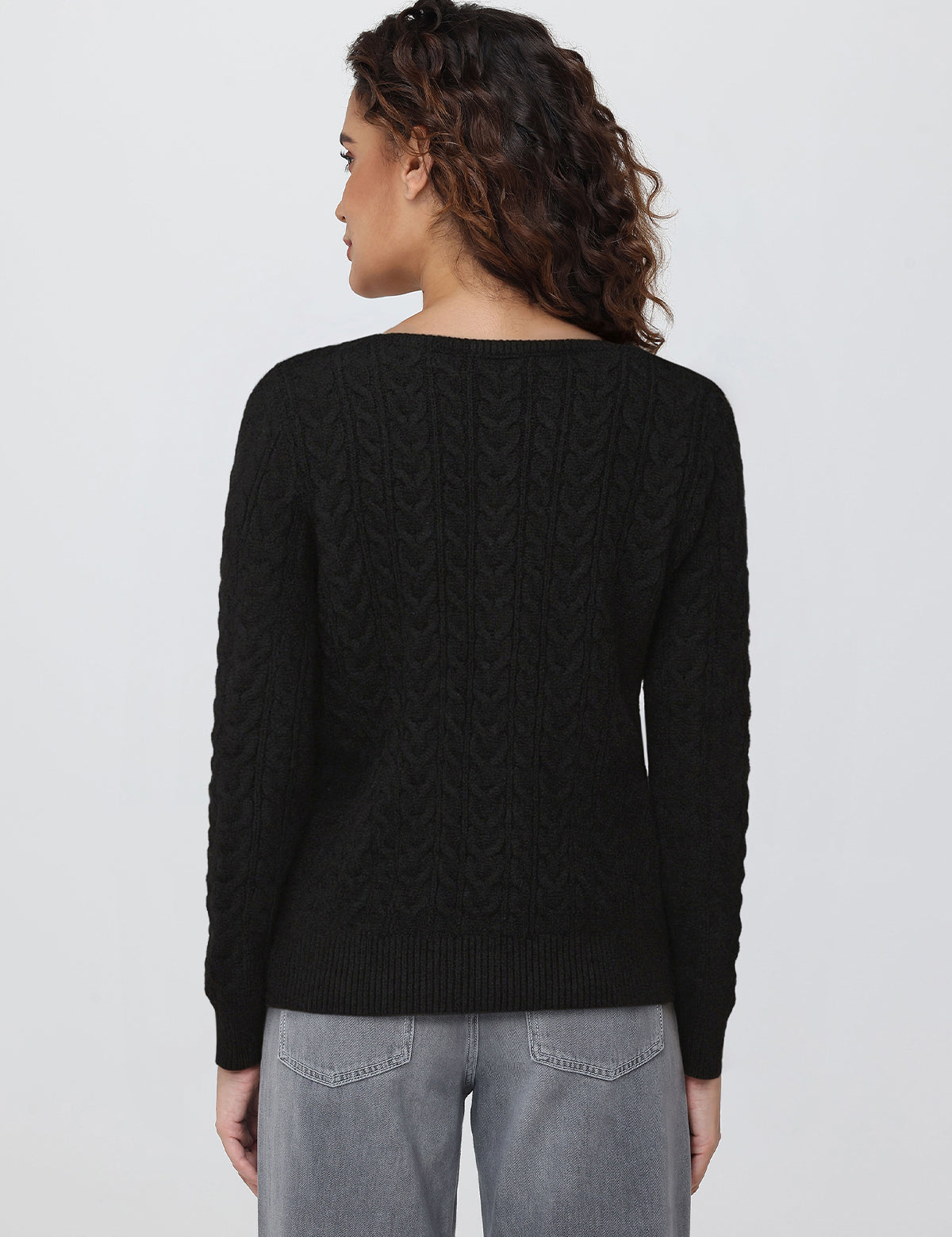 Person wearing a black cable knit cardigan on a plain background