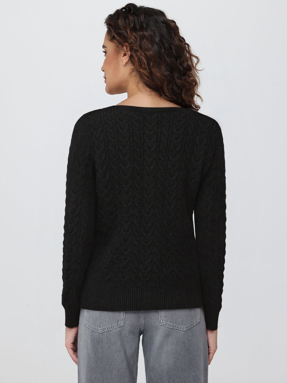 Person wearing a black cable knit cardigan on a plain background