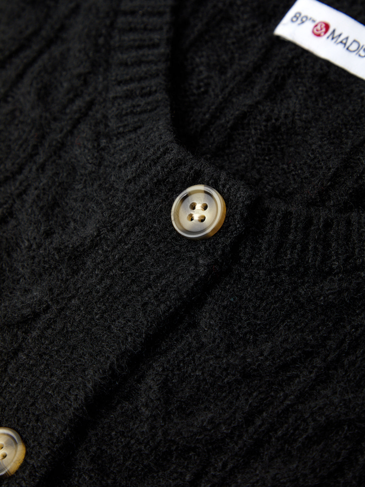 Close-up of a black cardigan with buttons and a brand label.