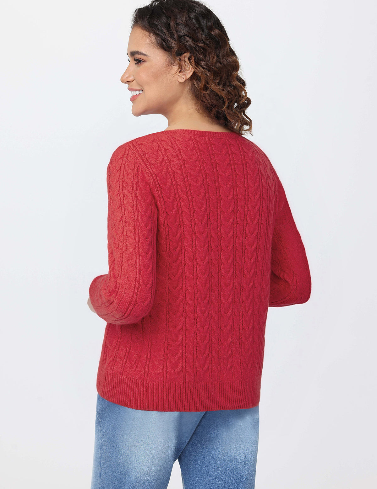 Woman wearing a red cable knit sweater and blue jeans on a white background