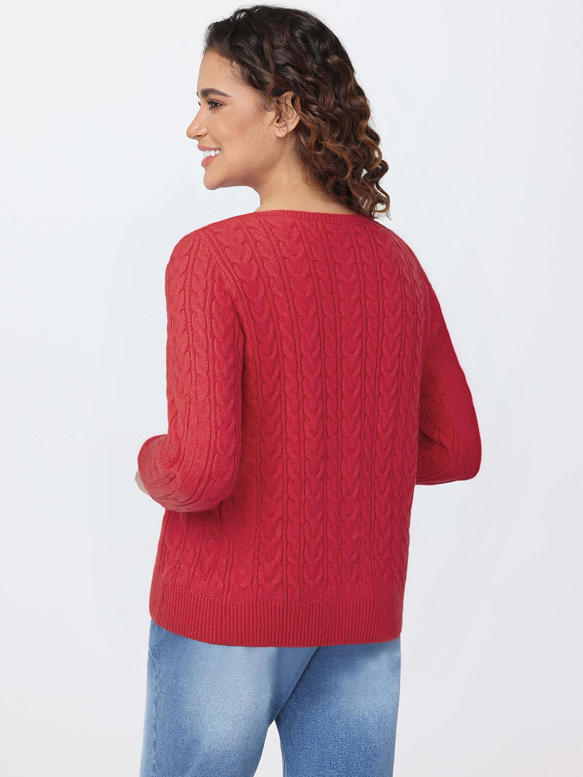 Woman wearing a red cable knit sweater and blue jeans on a white background