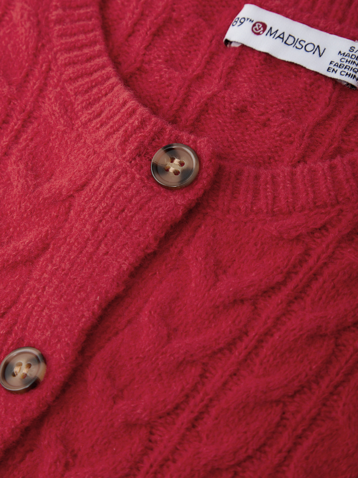 Close-up of a red cable knit sweater with a brand label.