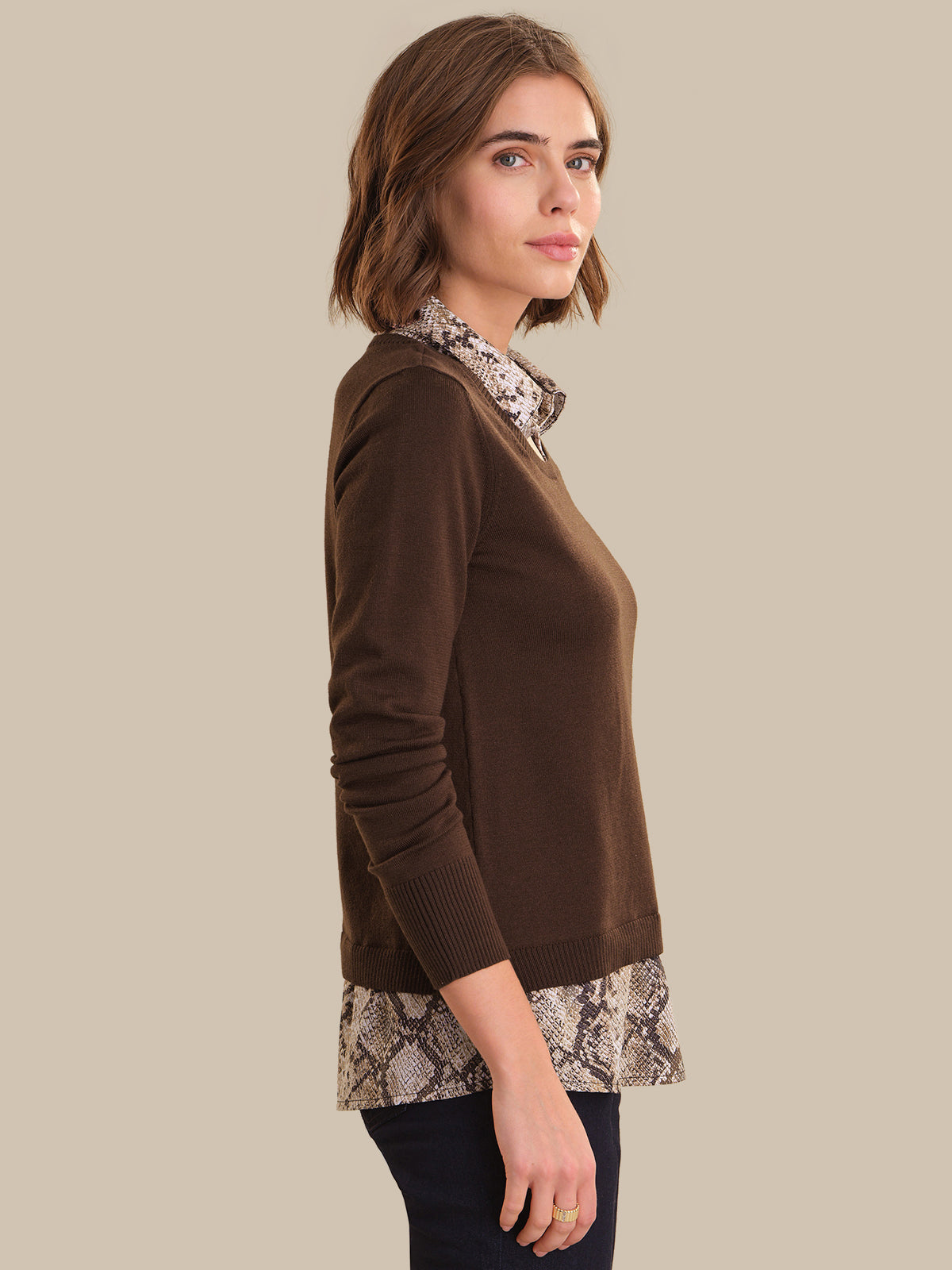 Woman wearing a brown sweater with patterned trim on a beige background