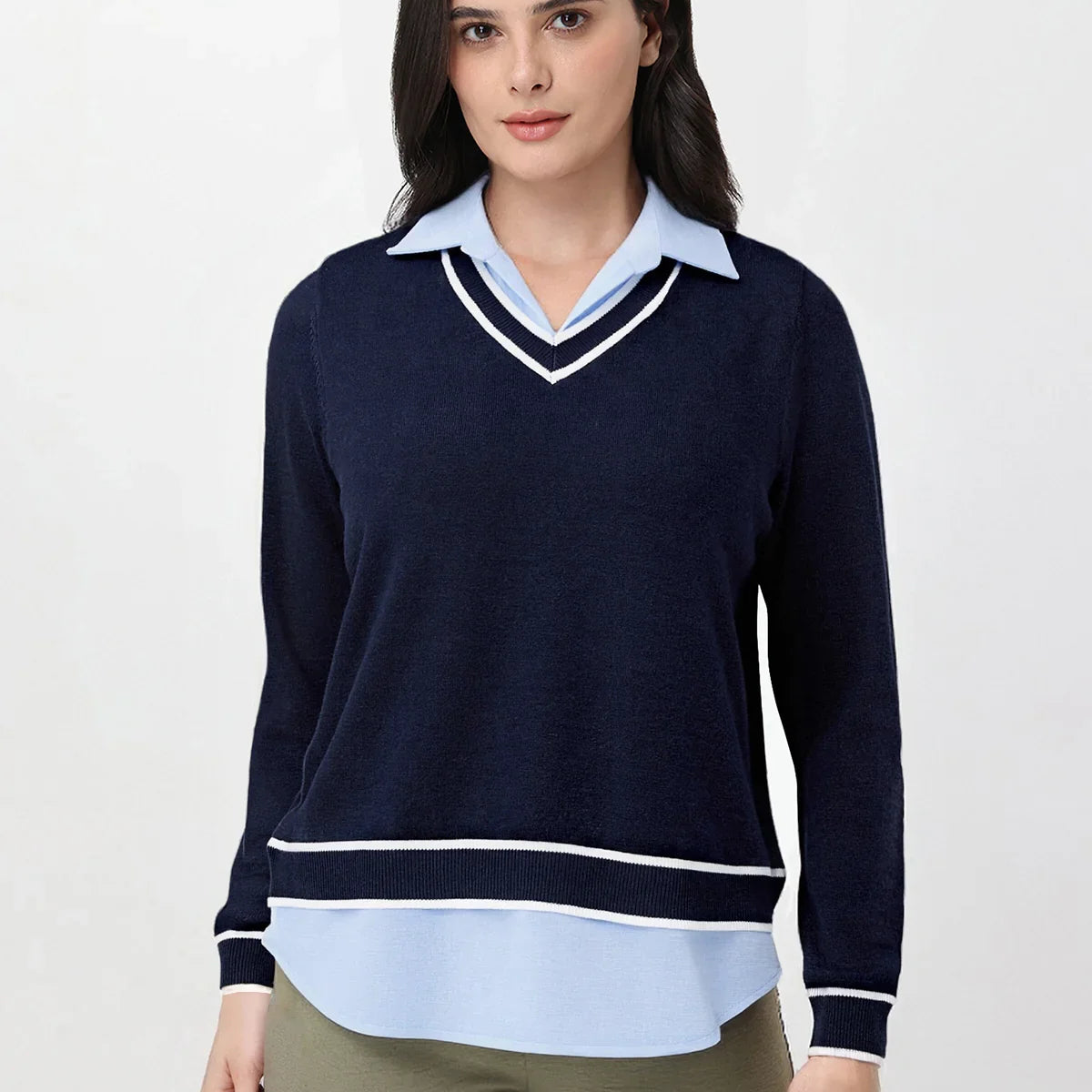 Woman wearing a navy sweater over a light blue shirt with beige pants on a white background