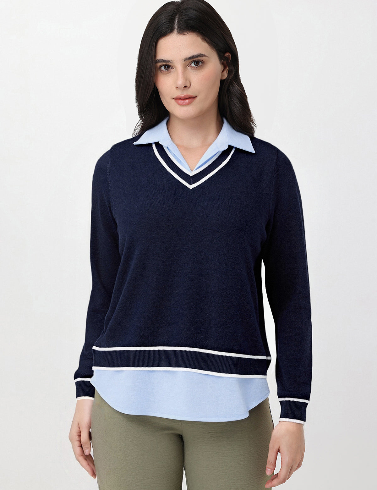 Woman wearing a navy sweater over a light blue shirt with beige pants on a white background