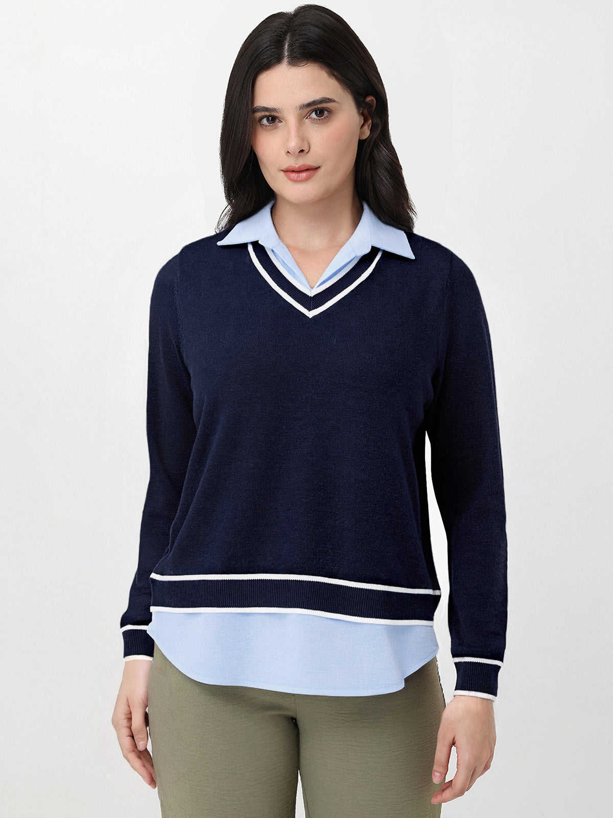 Woman wearing a navy sweater over a light blue shirt with beige pants on a white background