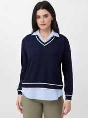 Woman wearing a navy sweater over a light blue shirt with beige pants on a white background