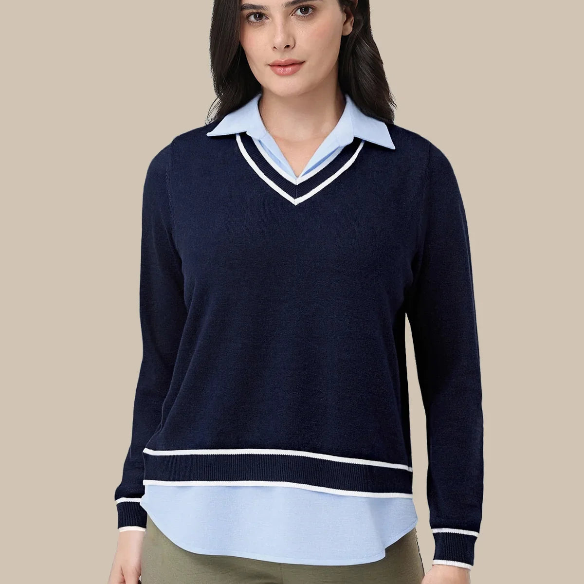 A woman modeling a navy blue long-sleeve knit sweater with a light blue collar and hem detail, styled with olive green pants against a solid beige background.