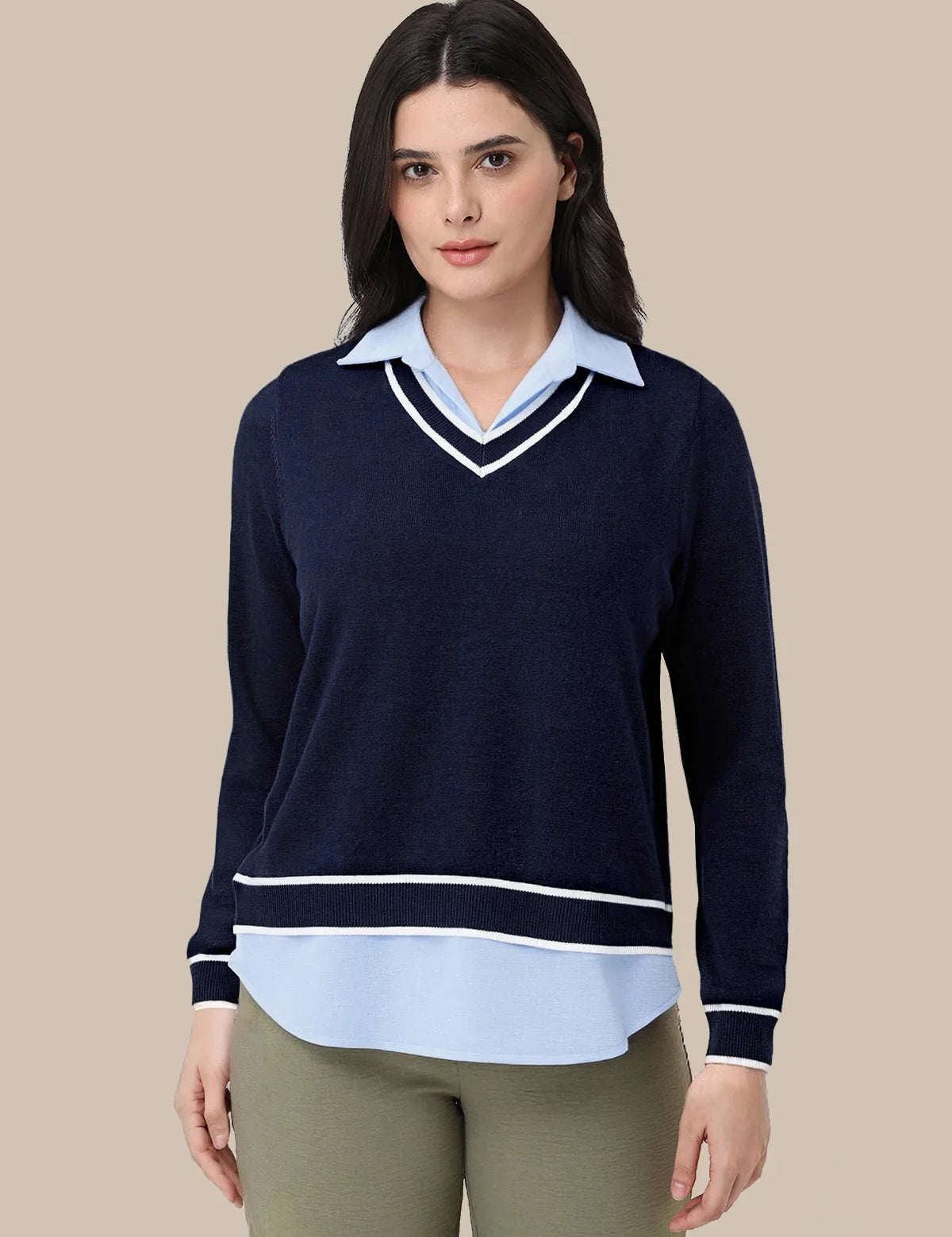 A woman modeling a navy blue long-sleeve knit sweater with a light blue collar and hem detail, styled with olive green pants against a solid beige background.