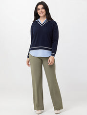 Woman wearing a navy sweater with a light blue shirt and green pants on a white background