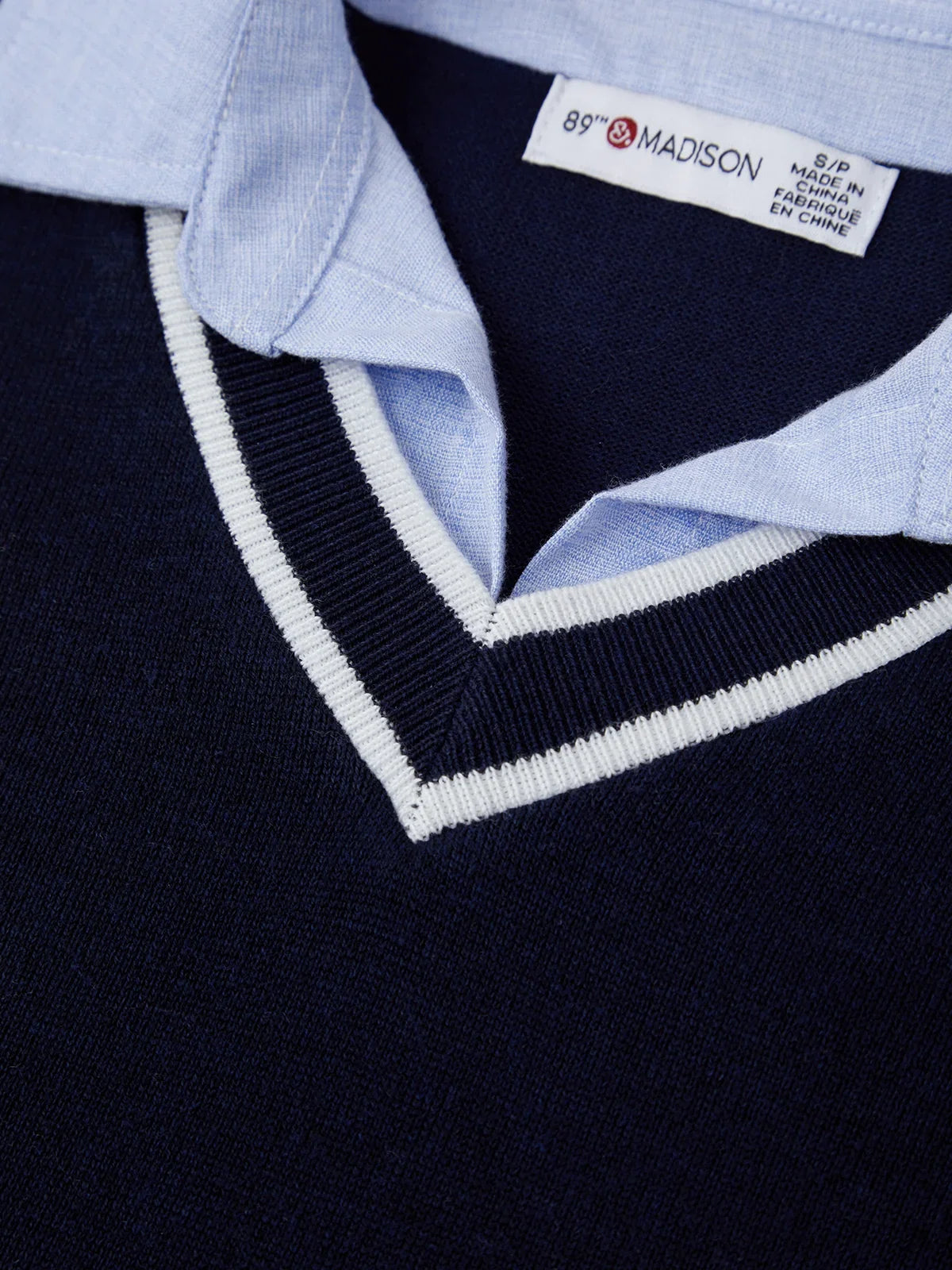 Close-up of a navy sweater with light blue collar and '87 & MADISON' label.