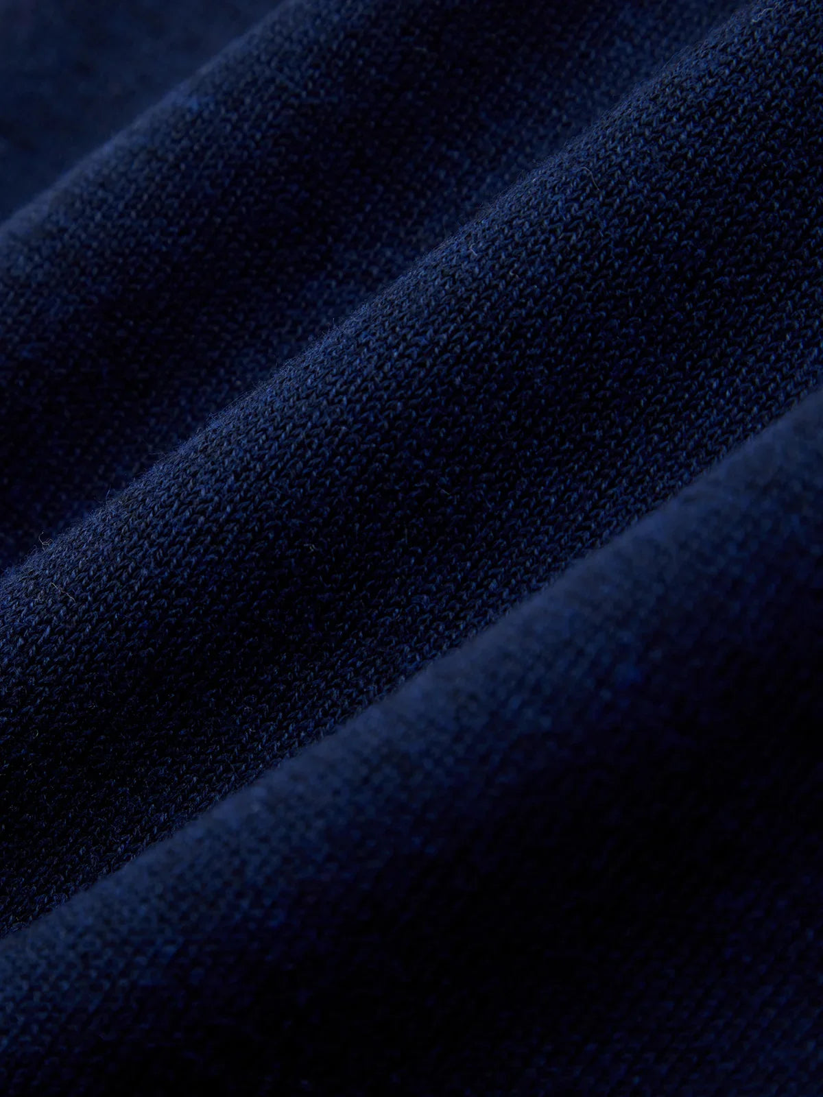 A close-up of dark navy blue knit fabric with soft diagonal folds showing the fine woven texture.