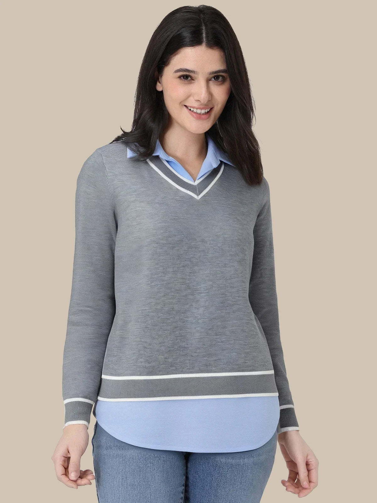 A woman modeling a gray long-sleeve knit sweater with a light blue shirt layered underneath, shown against a solid beige background.