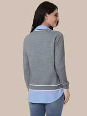 A woman shown from the back wearing a heather gray long-sleeve polo-style top with light blue contrast trim and a light blue underlayer, paired with blue jeans, against a solid beige background.