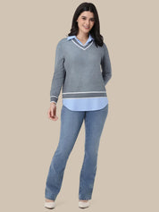 A woman modeling a gray long-sleeve sweater with a light blue V-neck collar and hem, paired with light blue jeans, against a solid beige background.