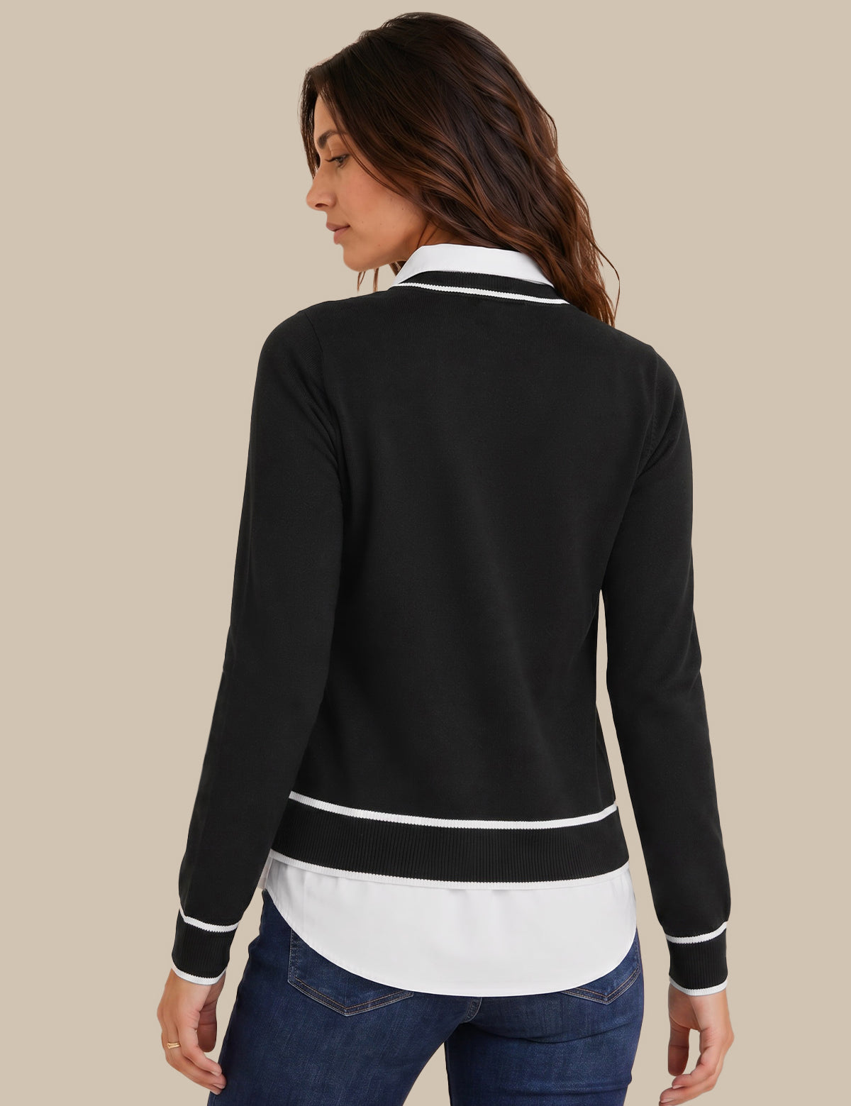 A woman shown from the back wearing a black long-sleeve knit top with white contrast trim at the collar, cuffs, and hem, paired with blue jeans, against a solid beige background.