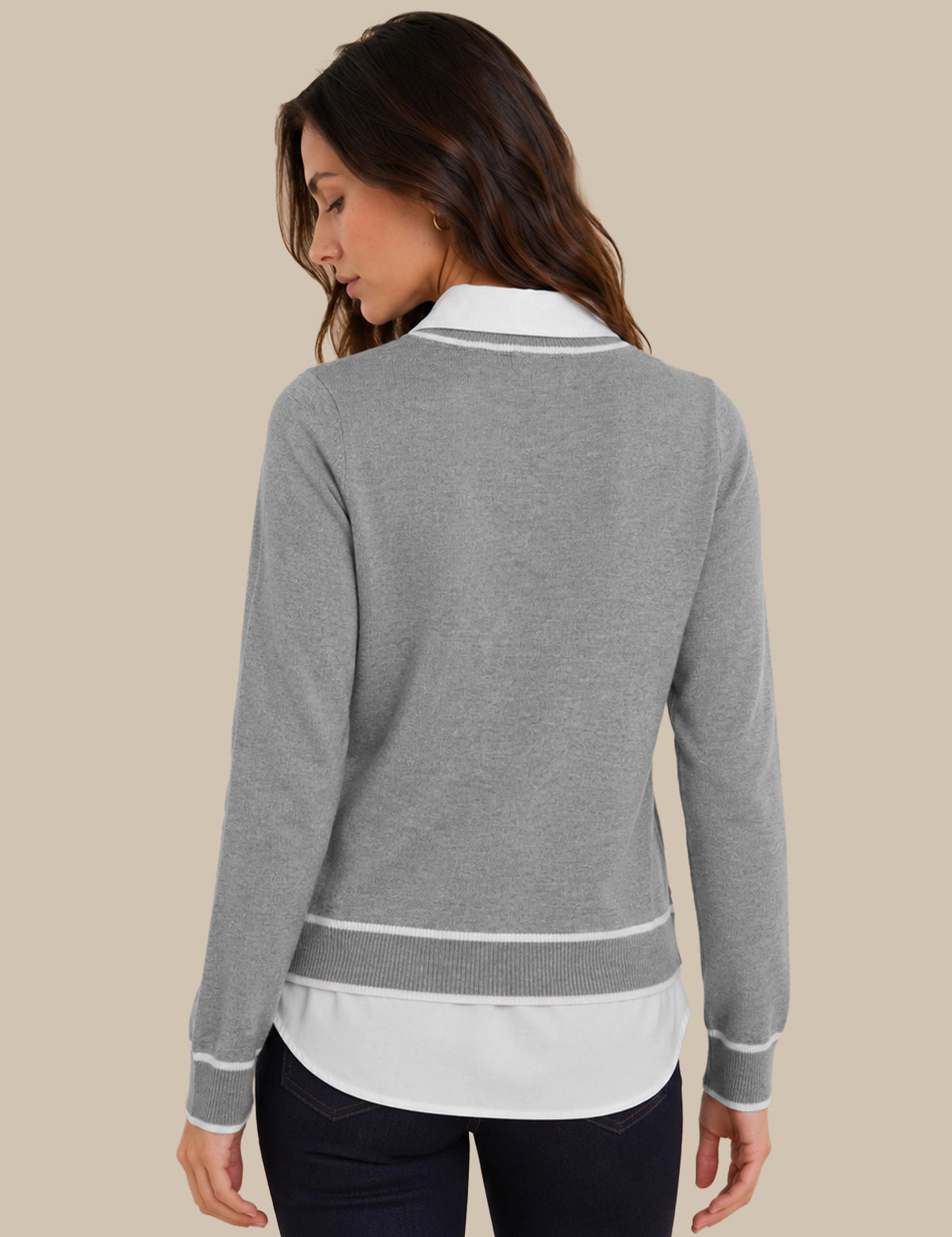 A woman shown from the back wearing a heather gray long-sleeve knit top with white contrast trim and a white underlayer, paired with dark pants, against a plain beige studio background.