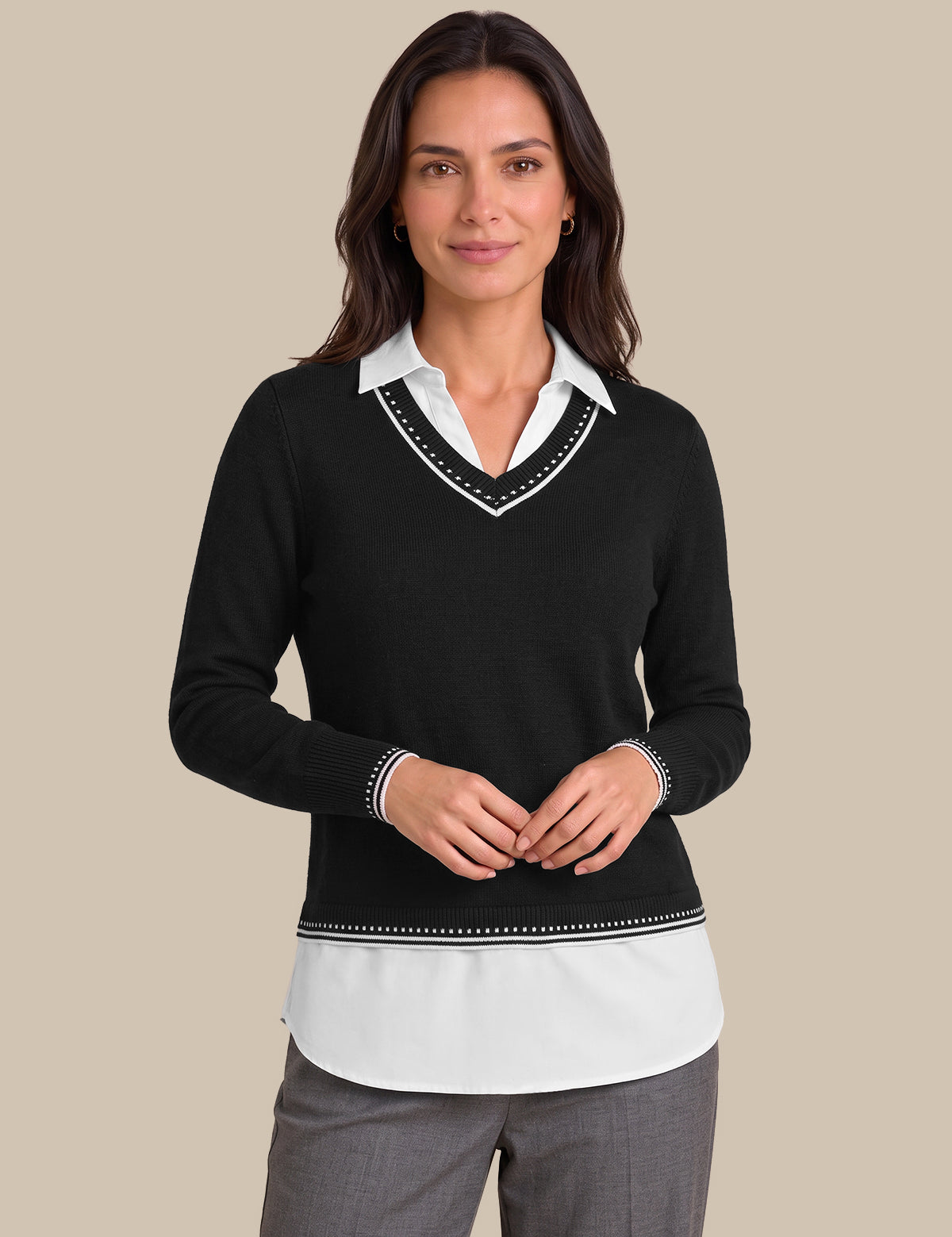 A woman modeling a black long-sleeve knit sweater with a white V-neck collar trim and a white underlayer visible at the hem and collar, paired with gray trousers, against a solid beige background.