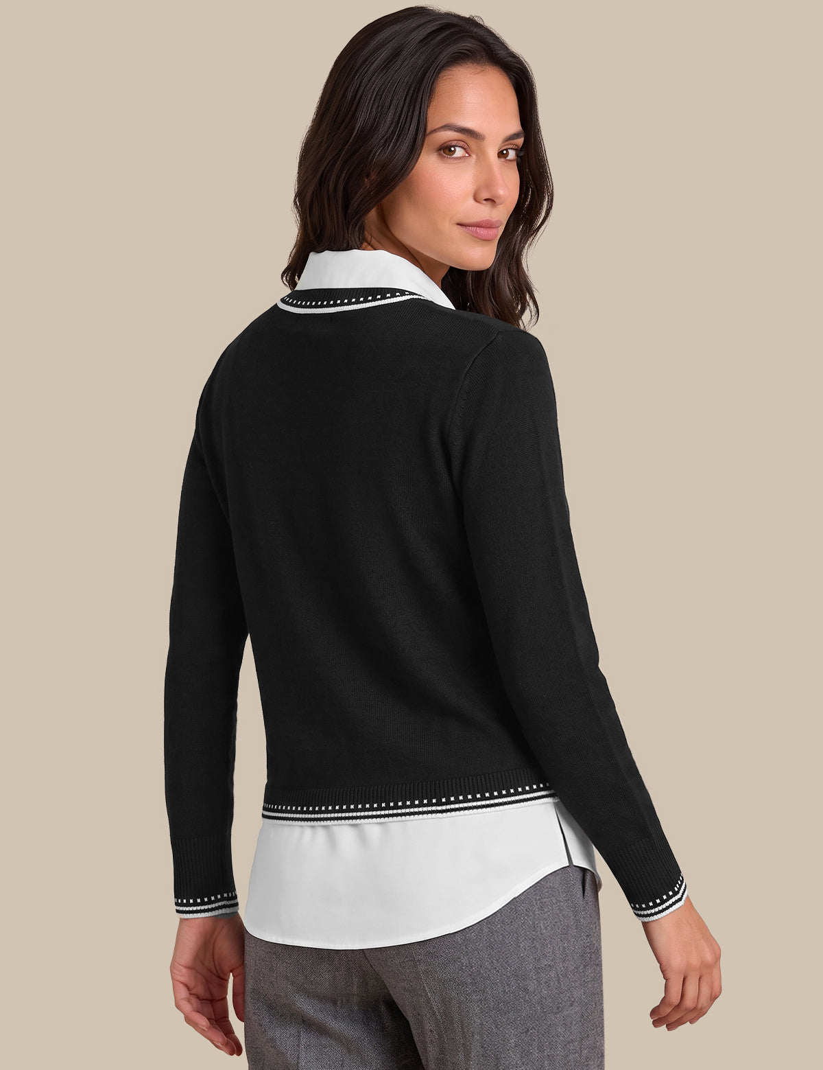A woman shown from the back wearing a black long-sleeve cardigan over a white collared shirt, paired with gray trousers, against a solid beige background.