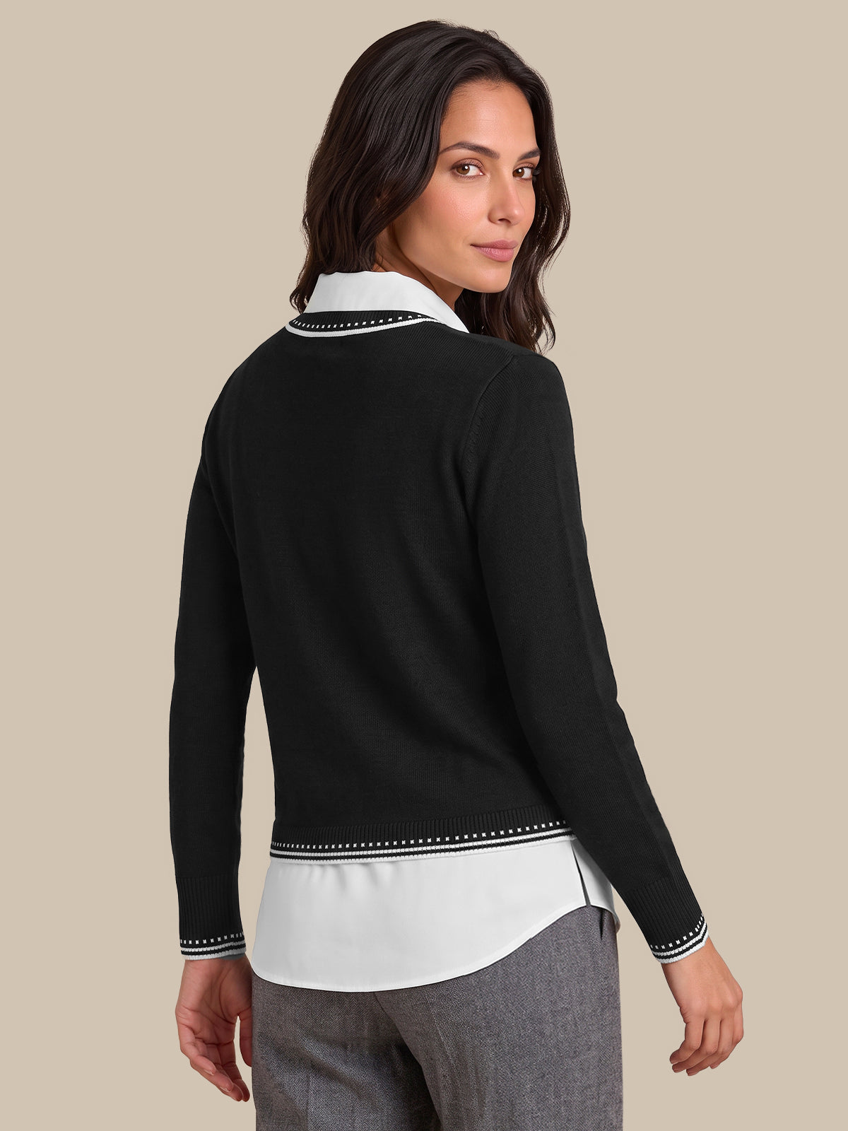 A woman shown from the back wearing a black long-sleeve cardigan over a white collared shirt, paired with gray trousers, against a solid beige background.