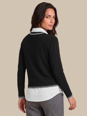 A woman shown from the back wearing a black long-sleeve cardigan over a white collared shirt, paired with gray trousers, against a solid beige background.