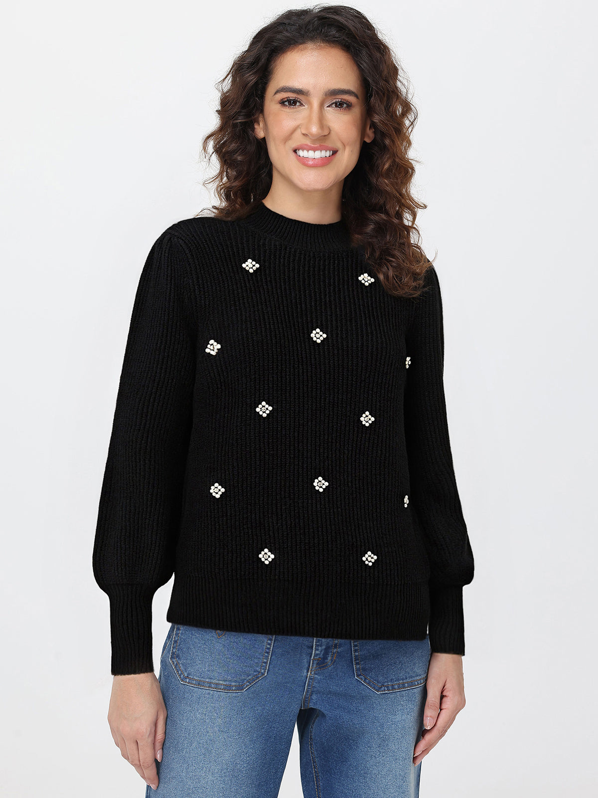 Woman wearing a black sweater with white embellishments on a plain background