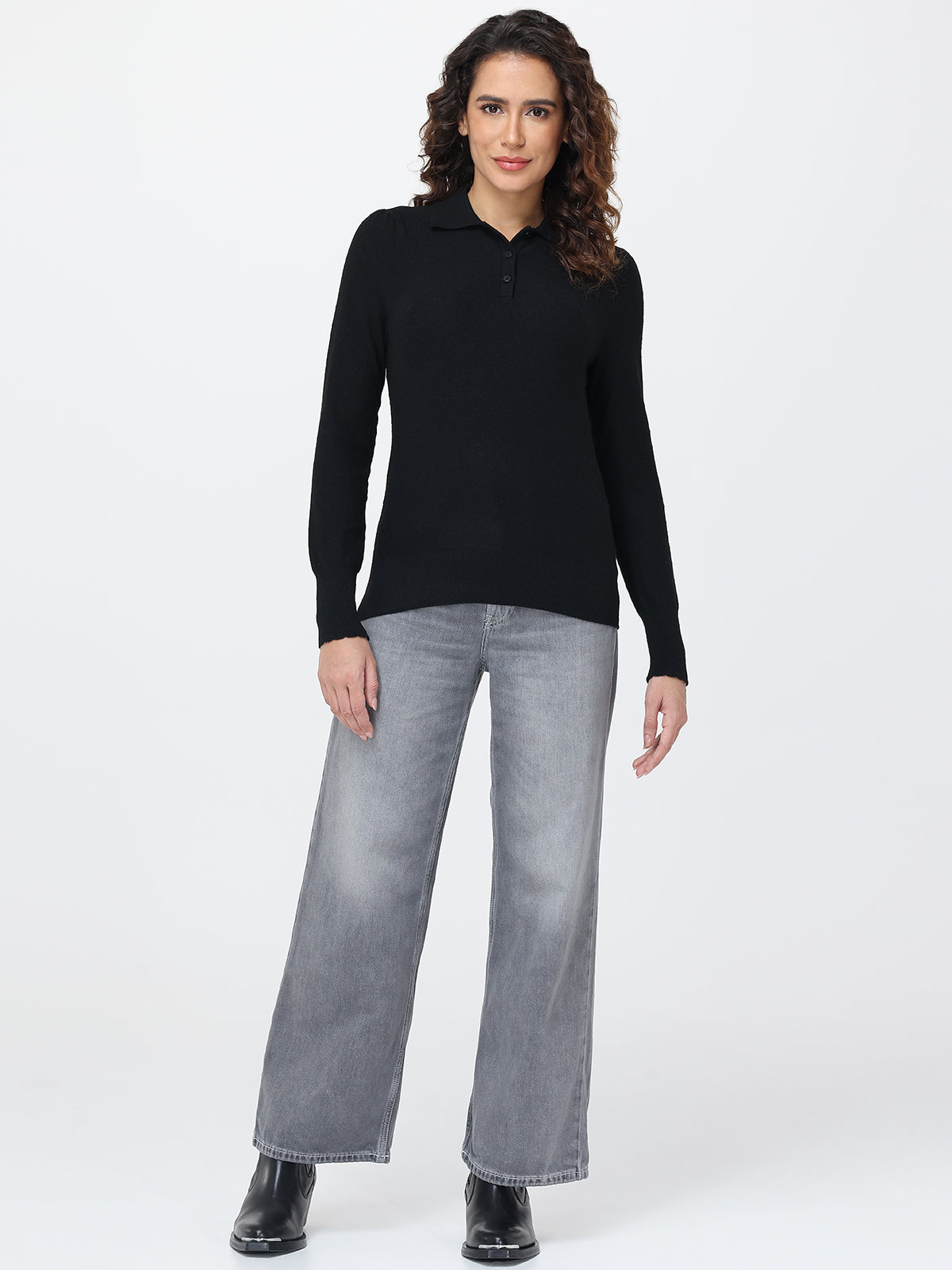 Woman wearing a black long-sleeve top and gray jeans on a white background