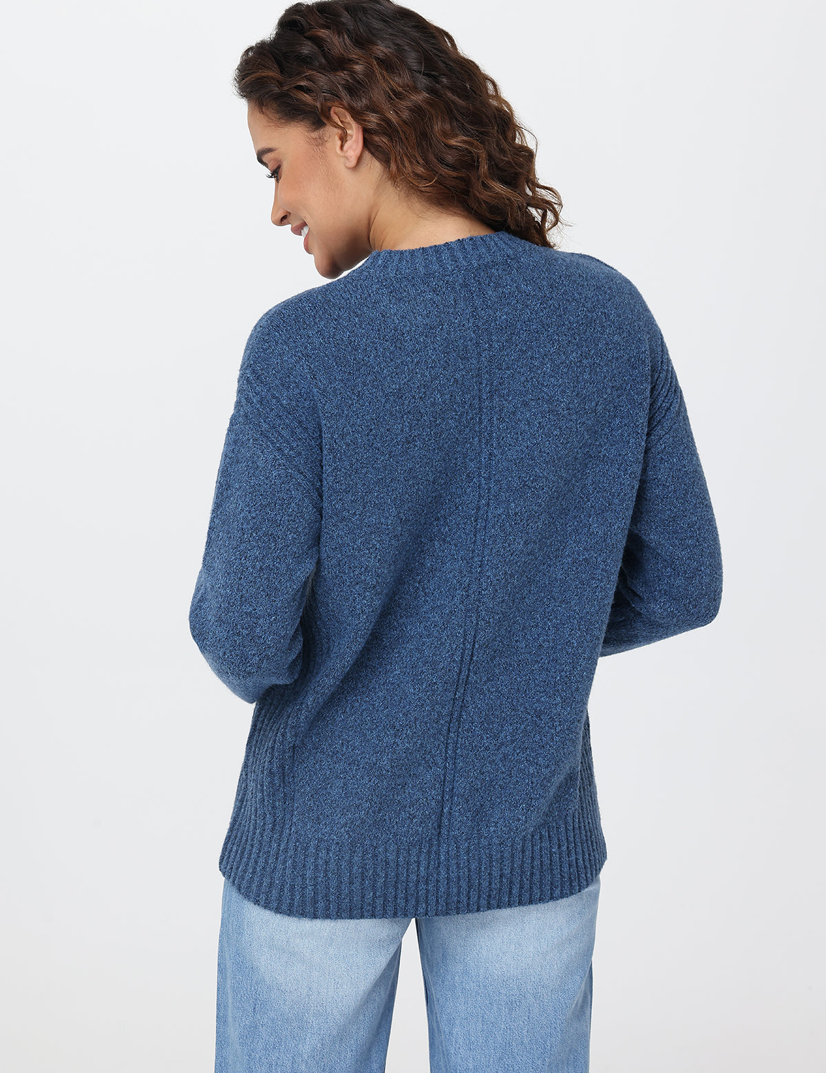 Woman wearing a blue sweater and light blue jeans on a white background