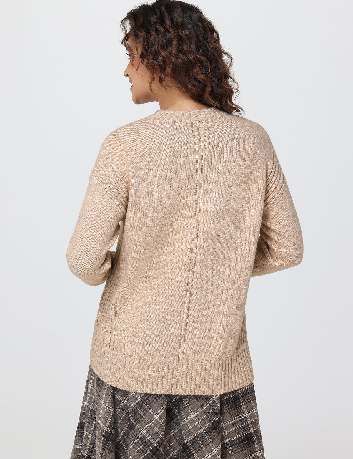 Woman wearing a beige sweater and plaid skirt on a white background