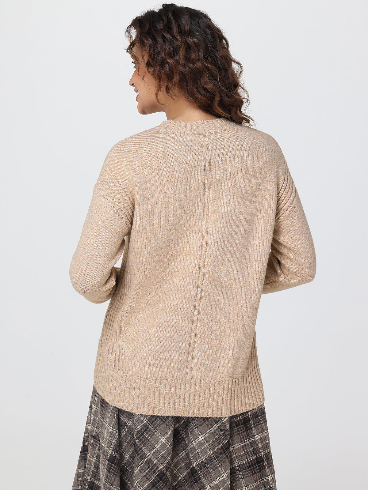 Woman wearing a beige sweater and plaid skirt on a white background