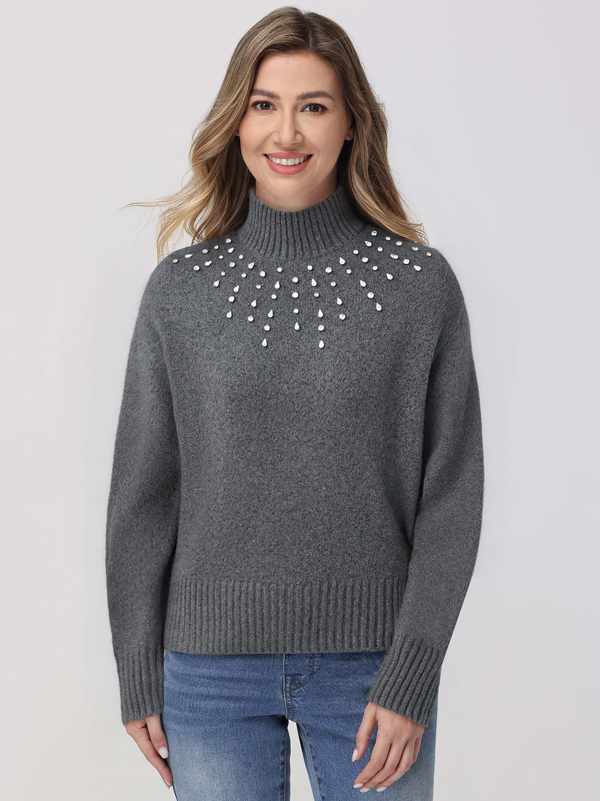 Woman wearing a gray sweater with pearl embellishments on a plain background