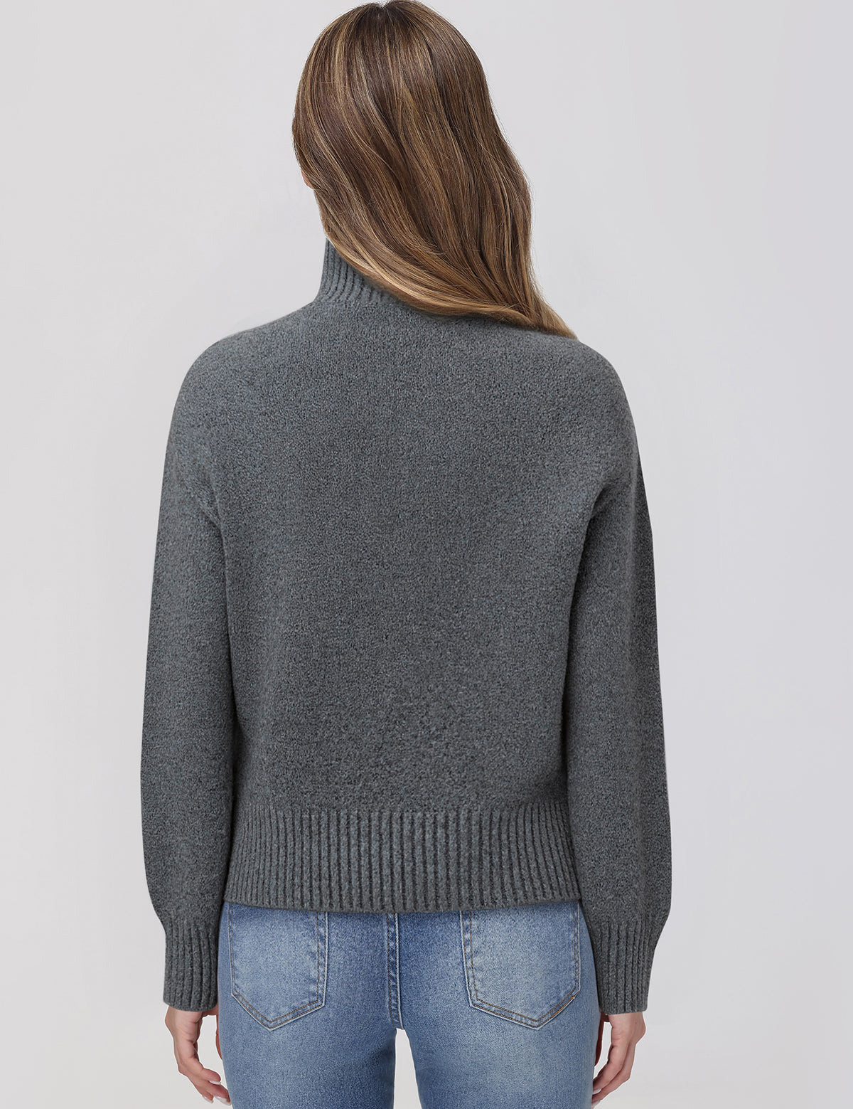 Person wearing a gray sweater and blue jeans on a light gray background