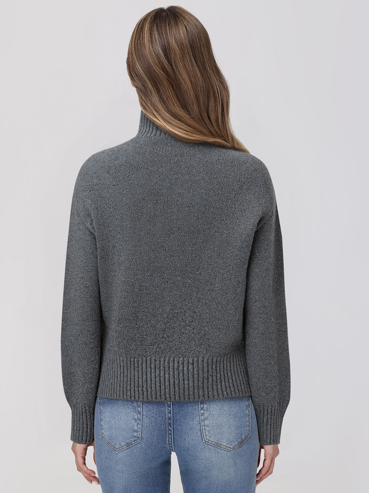 Person wearing a gray sweater and blue jeans on a light gray background