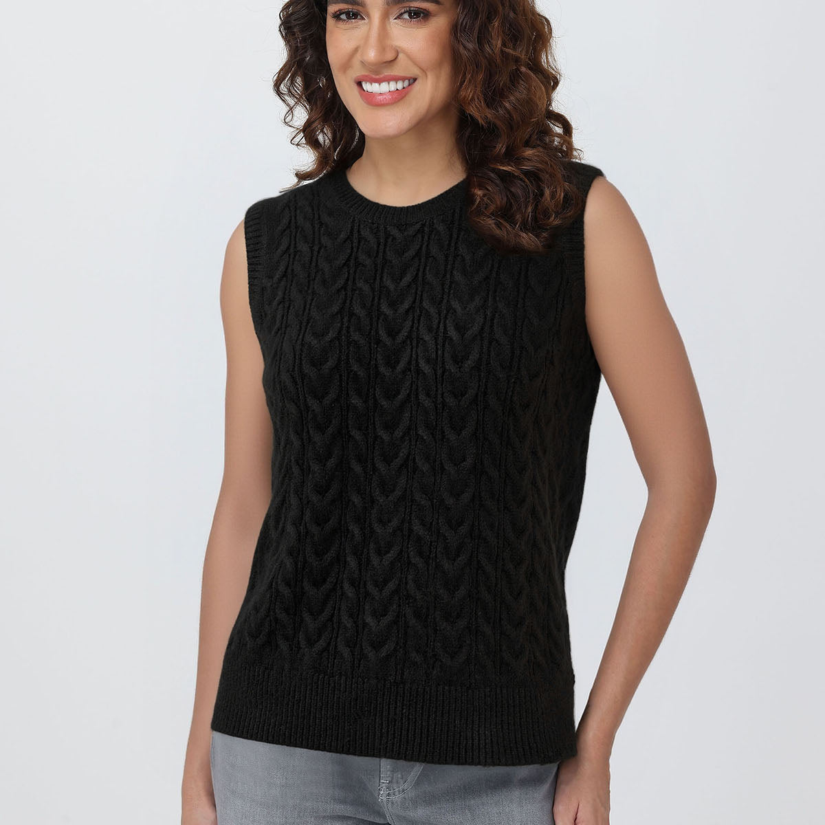 Woman wearing a black sleeveless knitted top against a plain background