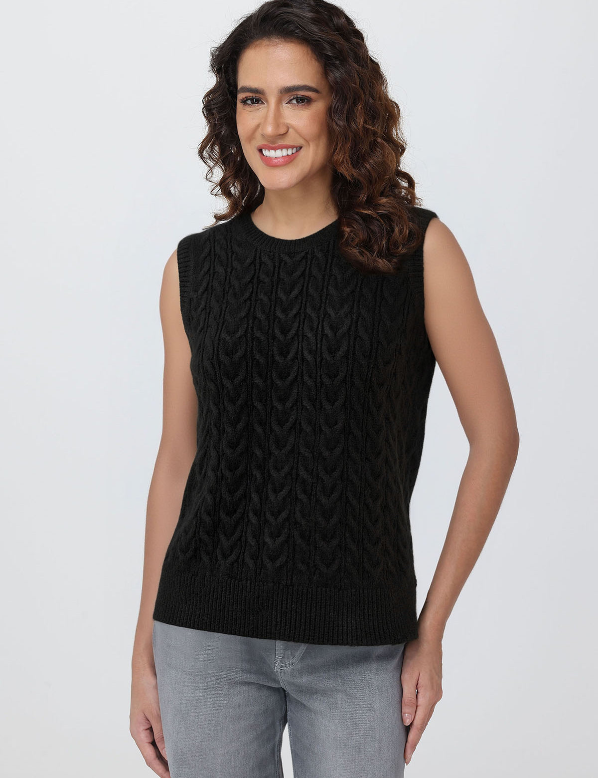 Woman wearing a black sleeveless knitted top against a plain background