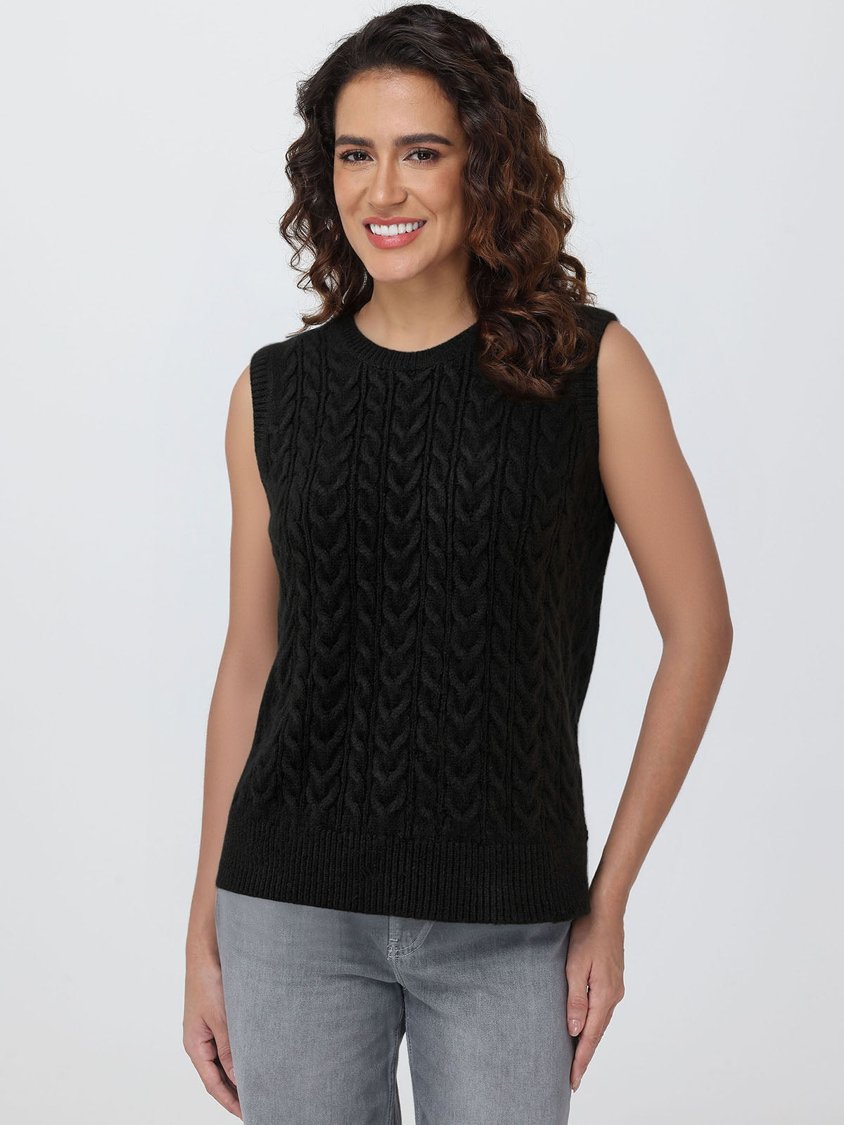 Woman wearing a black sleeveless knitted top against a plain background