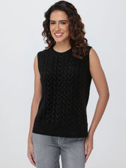 Woman wearing a black sleeveless knitted top against a plain background
