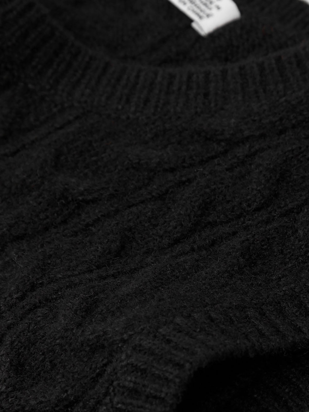 Close-up of a black cable knit sweater with a brand tag.