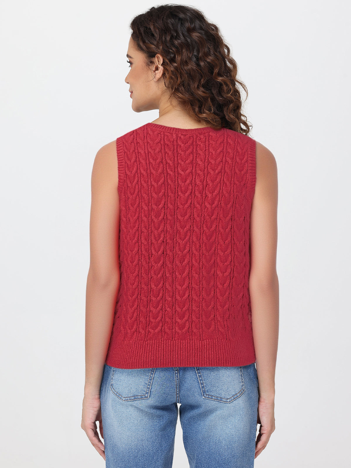 Woman wearing a red knitted sleeveless top and blue jeans on a white background