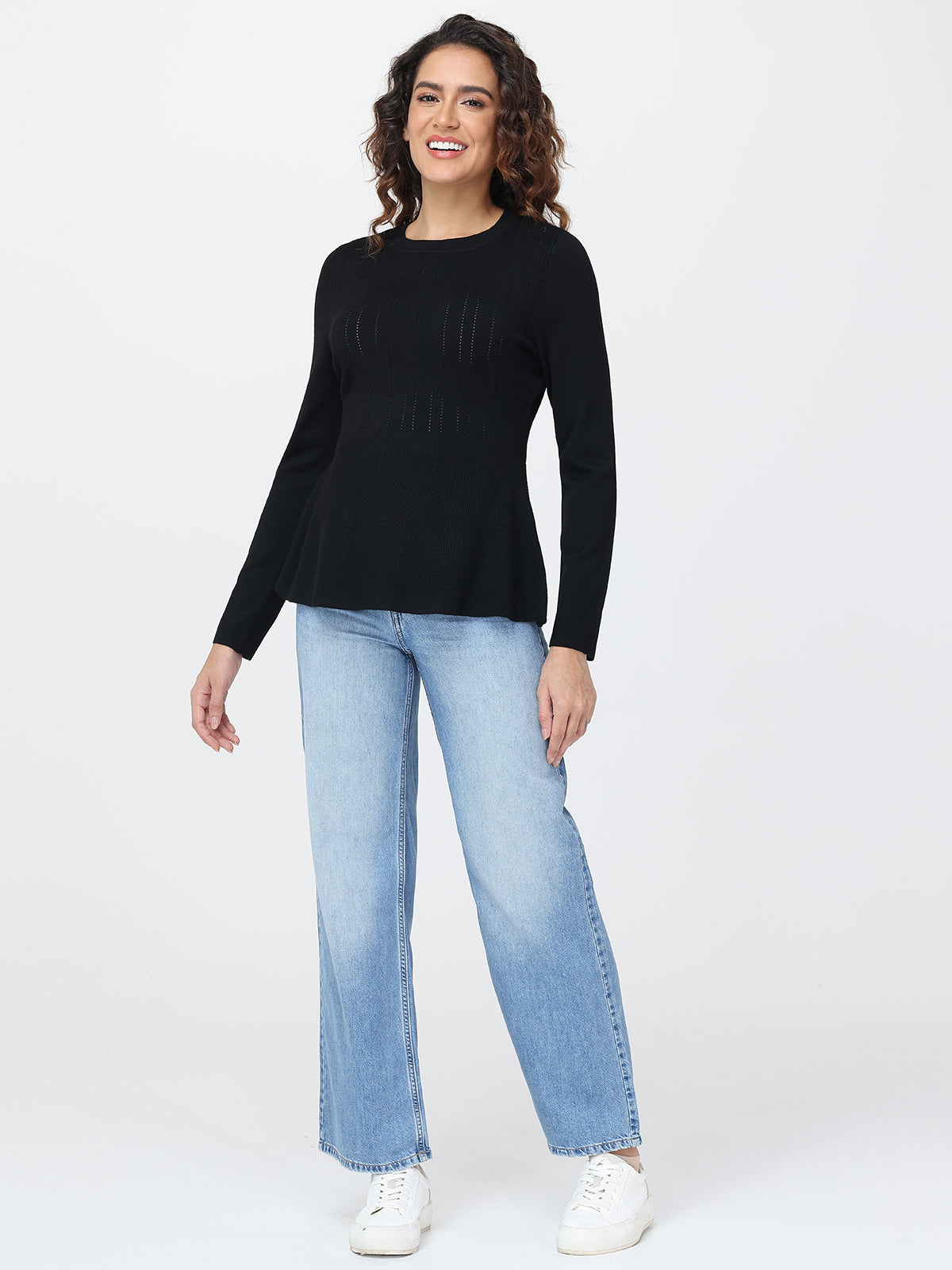 Woman wearing a black long-sleeve top and light blue jeans on a white background