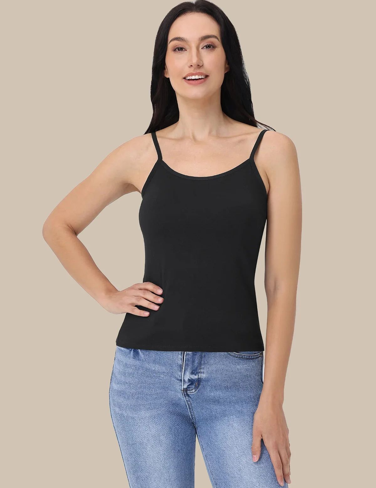 A woman modeling a black spaghetti-strap camisole tank top paired with light blue jeans, set against a solid beige background.