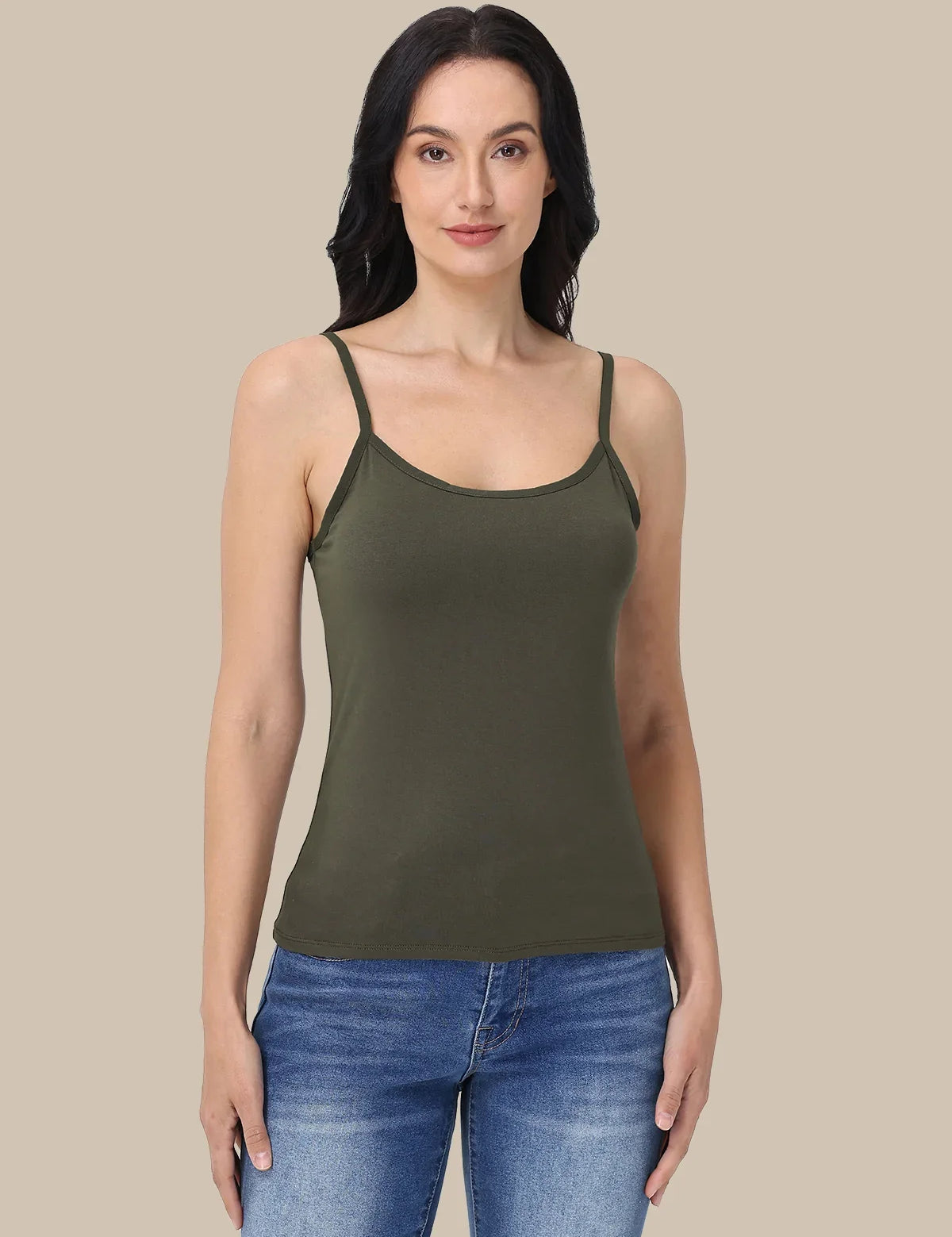 A woman modeling an olive green spaghetti-strap tank top paired with blue jeans, set against a solid beige background.