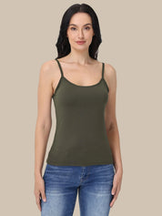 A woman modeling an olive green spaghetti-strap tank top paired with blue jeans, set against a solid beige background.