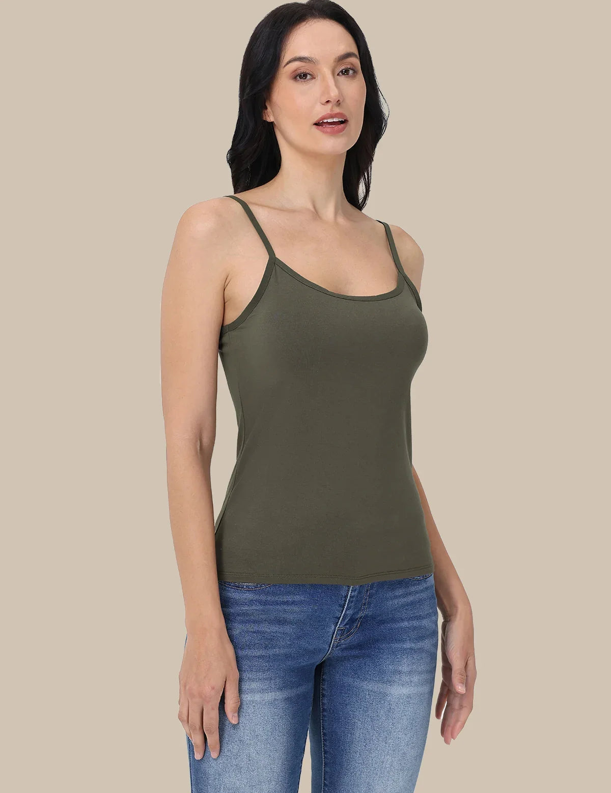 A woman modeling an olive green ribbed camisole tank top with thin shoulder straps, paired with blue jeans, against a solid beige background.